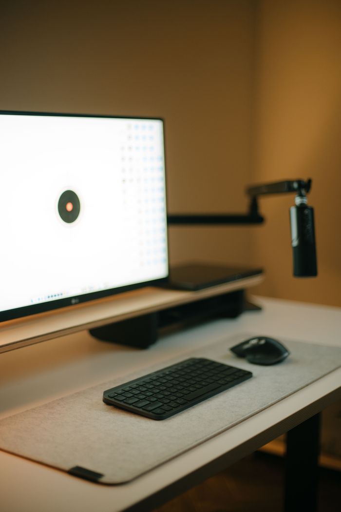 A sleek home office setup featuring a computer, keyboard, mouse, and microphone arm on a desk.